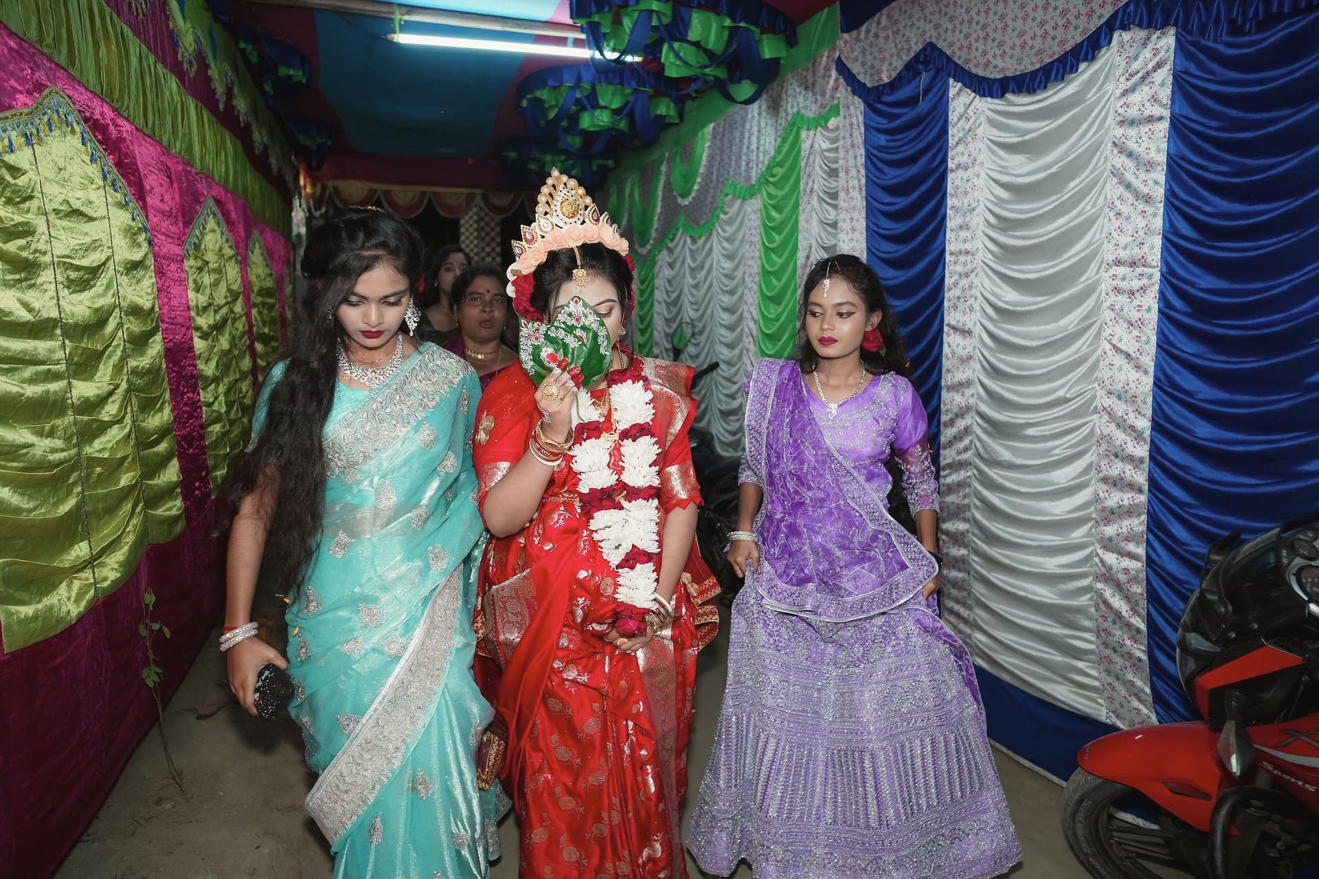 The bride walking in with women at her side along a draped passage