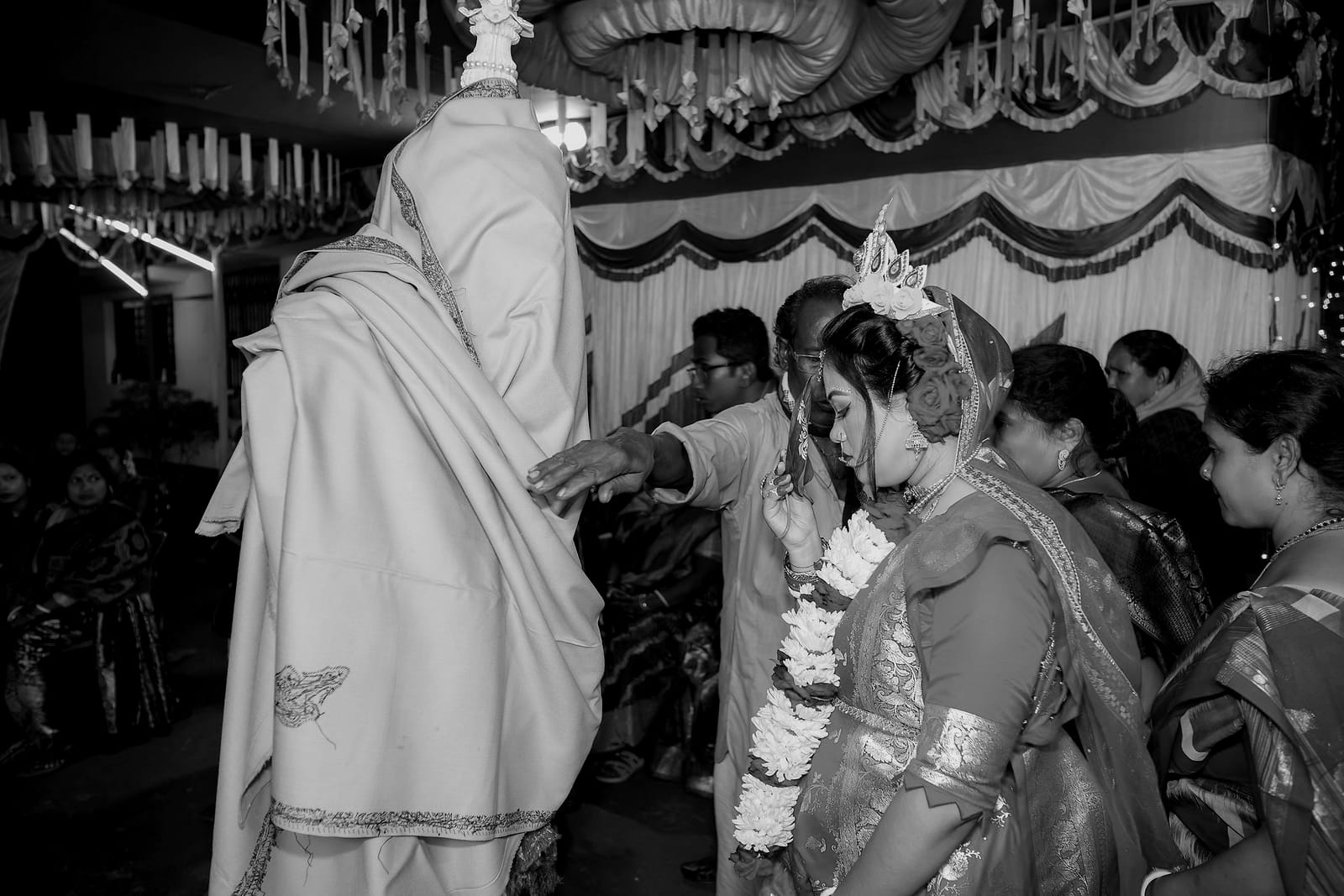 The groom in a cream shawl facing the bride among onlookers