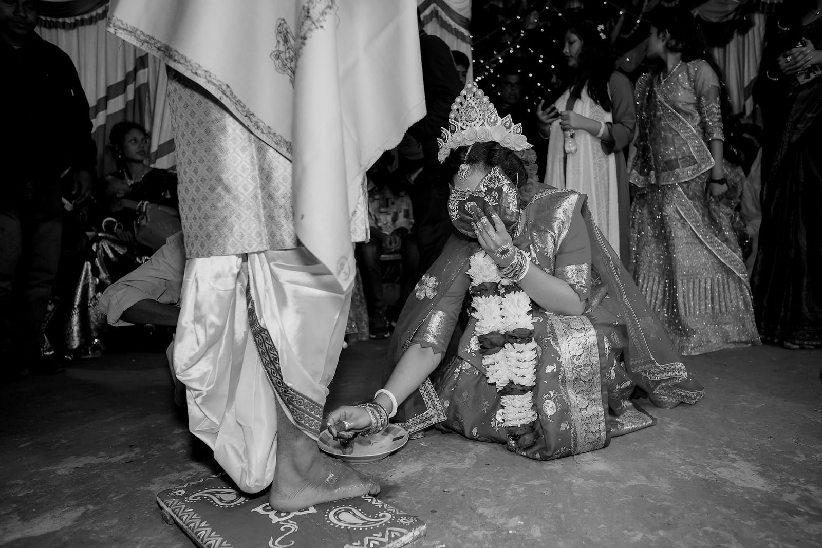 The bride on a red mat with the groom standing, guests behind them