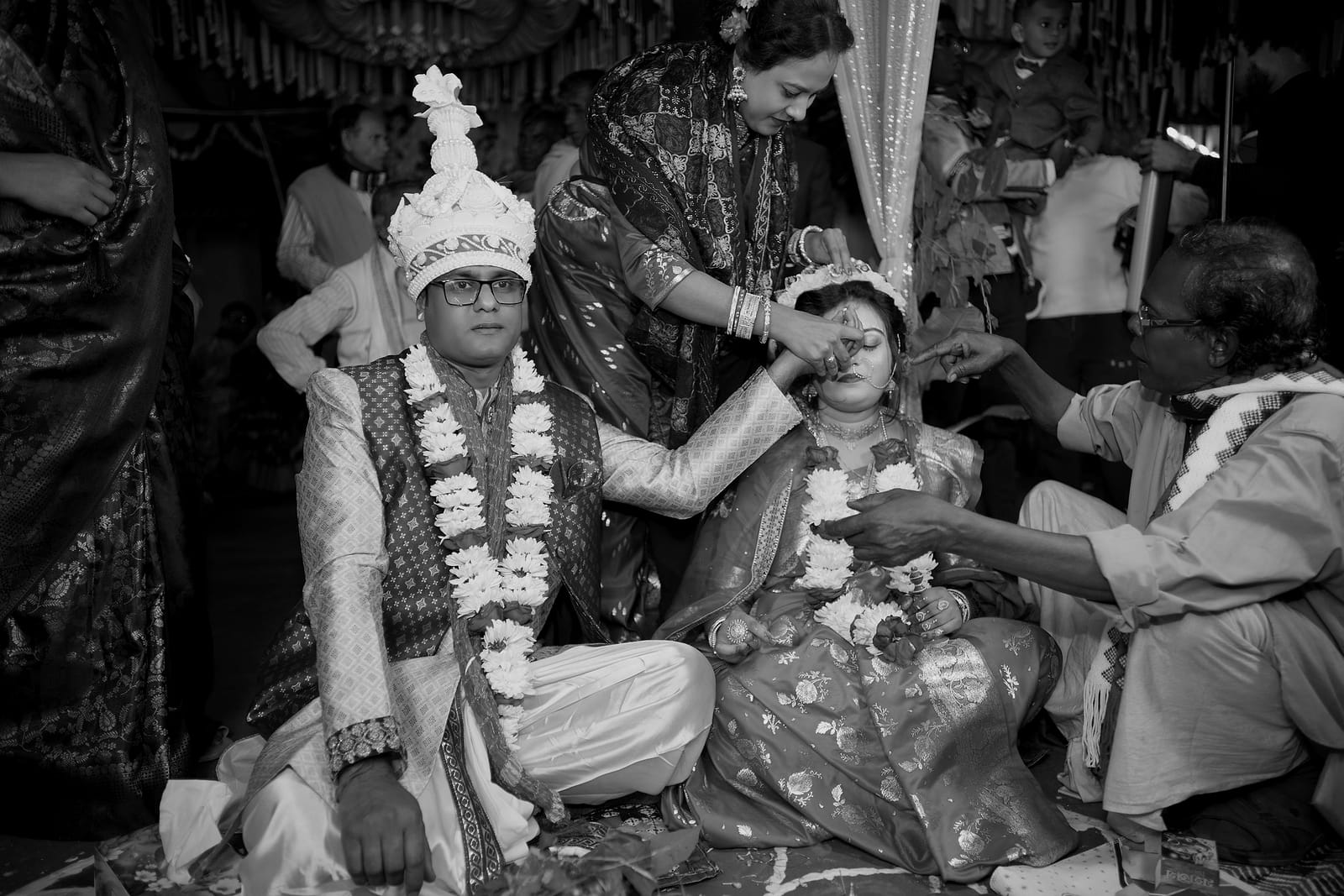 Relatives' hands reaching toward the groom as the couple sit in garlands