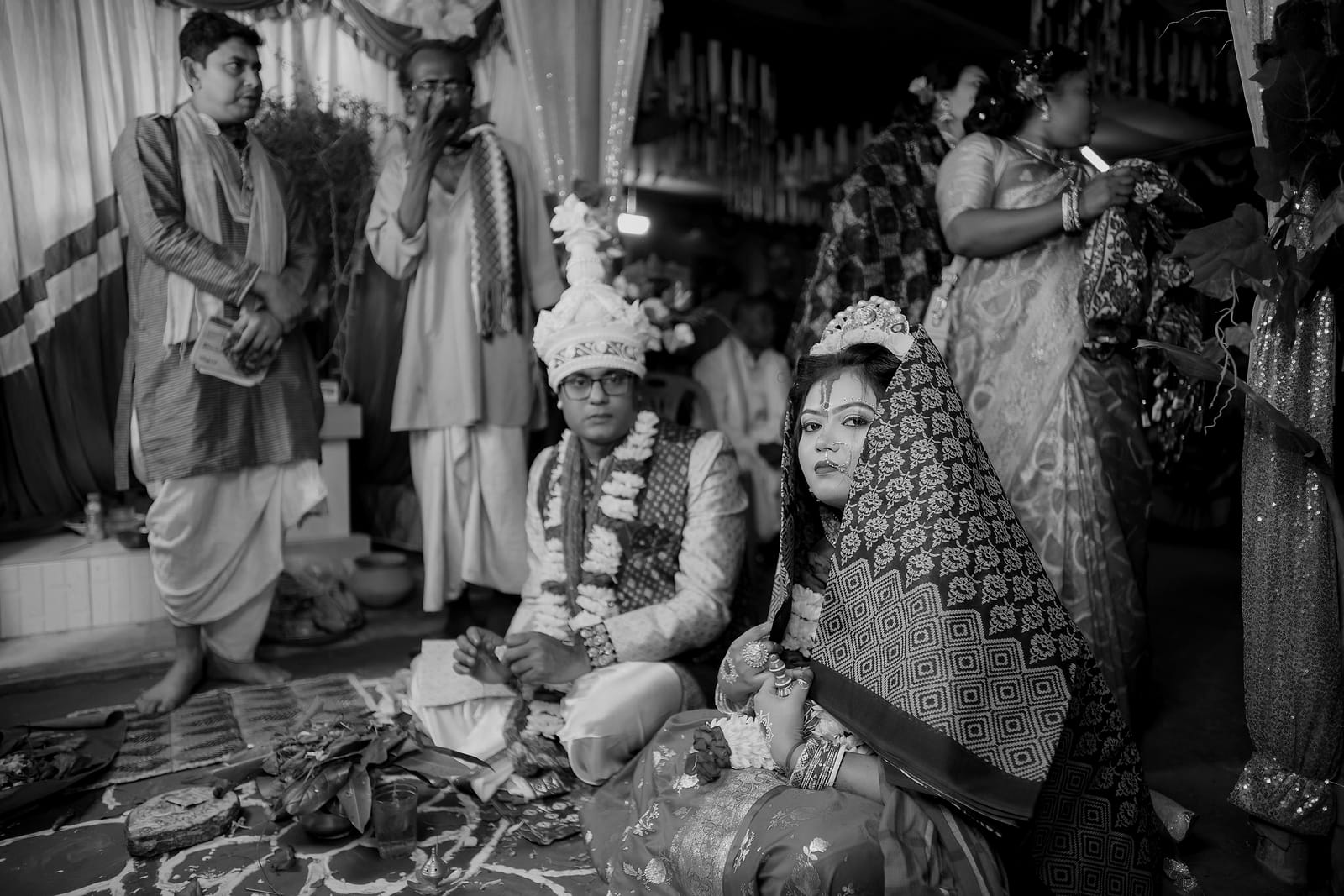 The seated couple in garlands, relatives leaning in around them